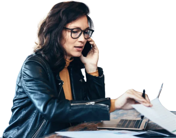 Woman wearing glasses using a phone while reviewing documents.