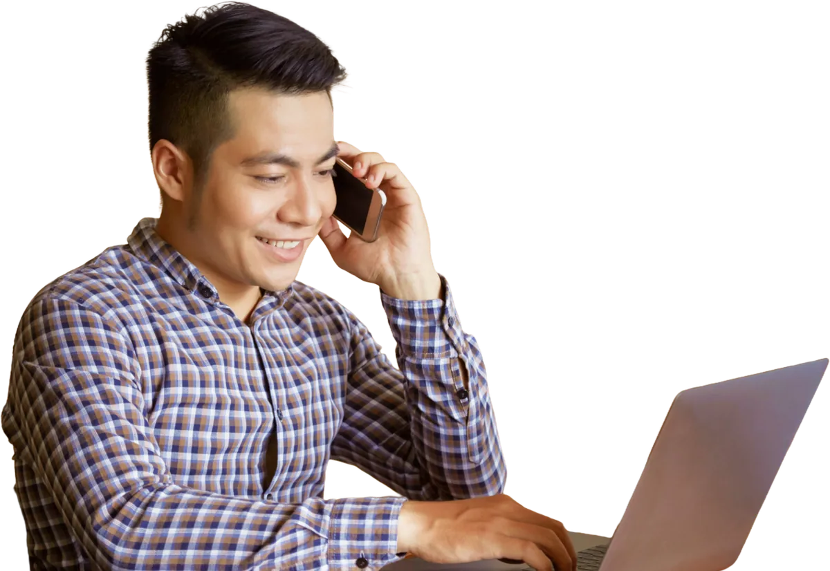 Man in a checked shirt using a phone beside a laptop.